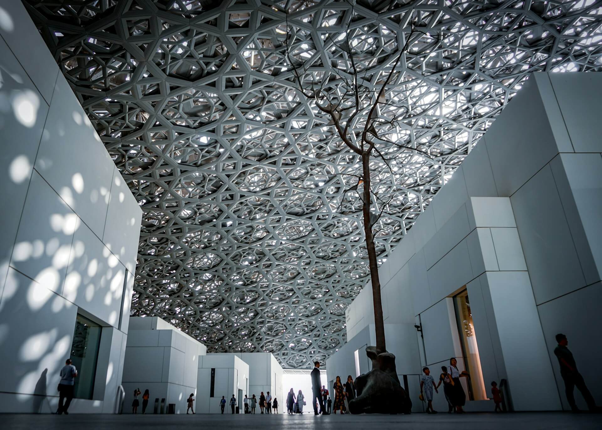 Light filtering through the latticed dome of the Louvre Abu Dhabi over the galleries and water